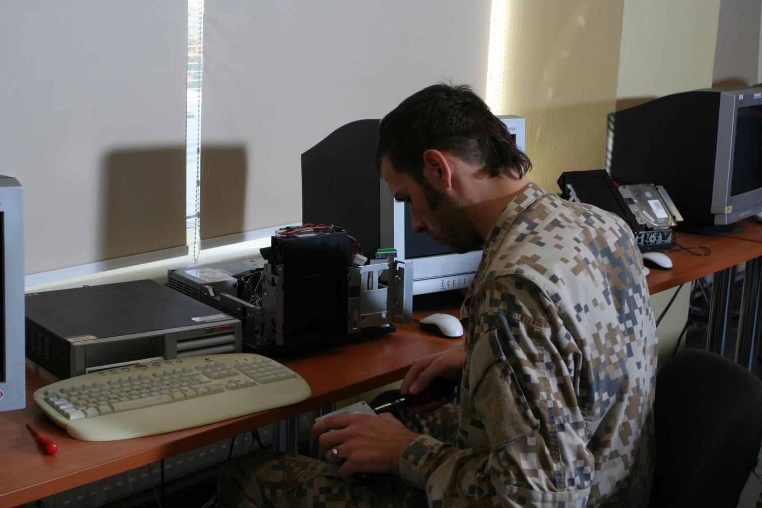 Št.vsrž.Ivars Šmits lauka formas tērpā, sēžot pie galda gatavo datorus apmācībai