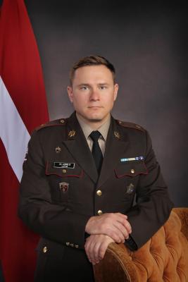 Andris Ločmelis uz Latvijas karoga fona svētku formas tērpā