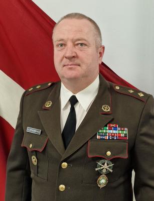 Pulkvežleitnants Vents Lapsenbergs svētku formas tērpā uz Latvijas karoga fona 