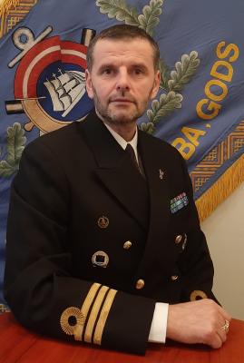 Attēlā redzams Jūras spēku mācību centra komandieris komandleitnants Kaspars Miezītis svētku formas tērpā, fonā - Jūras spēku mācību centra karogs