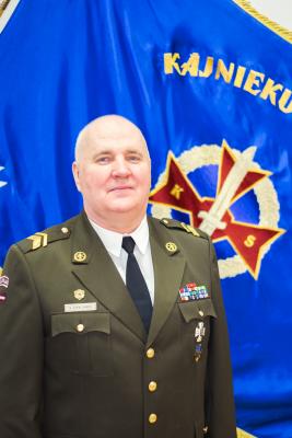 Bildē redzams štāba vvirsseržants Vilnis Pavlovičs. Kājnieku skolas virsseržants svētku formas tērpā uz Kājnieku skolas karoga fona